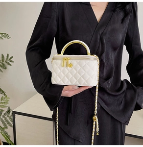Detail of white quilted mini bag with gold arch handle and floral zipper charm