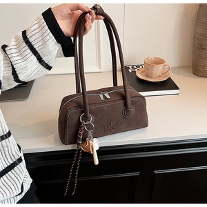Close-up of brown suede cylinder shoulder bag with embossed text and sports charms