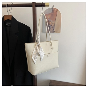 Detail of cream leather tote bag with a checkered silk scarf on dark wood hanger