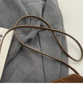 Detail of a brown leather shoulder strap with white contrast stitching on a crossbody bag