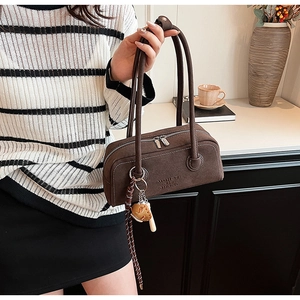 Detail of brown suede shoulder bag with baseball charm and metallic dual zippers