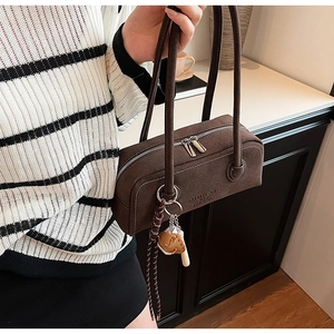 Close-up of brown suede cylindrical handbag featuring dual zippers and decorative charms