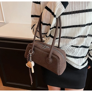 Detail of dark brown suede underarm bag with embossed text and baseball charm accessory