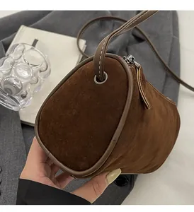 Detail of a brown suede cylinder crossbody bag with zipper and slim shoulder strap