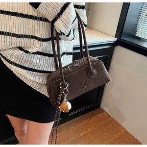 Detail of a dark brown suede underarm bag with an embossed logo and a decorative charm