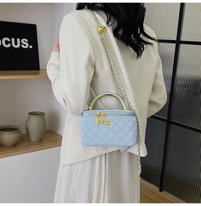 Detail of light blue quilted mini box bag with gold handle and adjustable ball chain