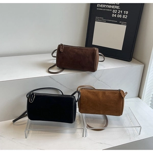 Close-up of minimalist cylindrical pillow bags in suede material with thin leather straps