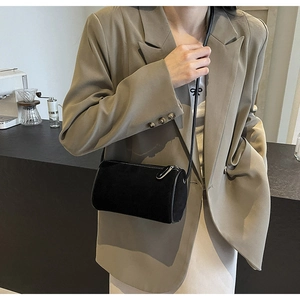 Detail of a black cylindrical crossbody bag in matte suede texture worn with a beige blazer