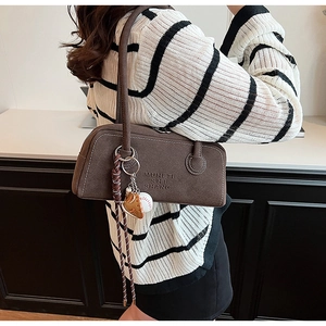 Detail of suede underarm bag with embossed text and a baseball glove keychain accessory