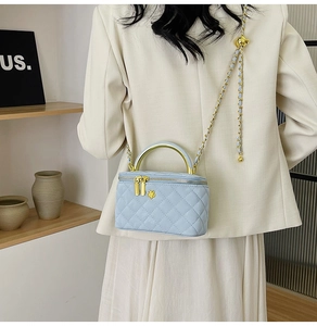 Detailed view of light blue quilted mini box bag with gold metal handle and chain strap
