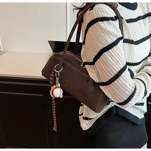 Close-up of a brown suede bowling bag with baseball charm and woven rope detail