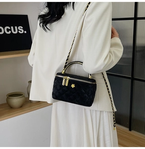 Detail of black quilted velvet bag with gold handle, chain strap, and floral ornament