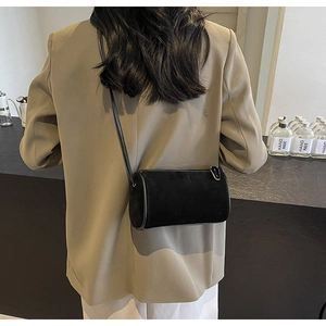 Close-up of black cylinder crossbody bag with white contrast stitching on suede texture