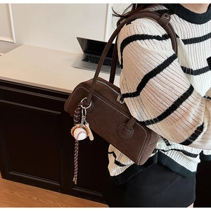 Detailed macro view of dark brown suede shoulder bag with baseball charm and relief text