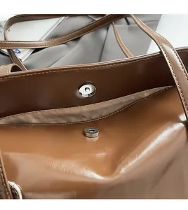 Close-up of brown glossy shoulder bag showing metallic magnetic buckle and inner zipper pocket