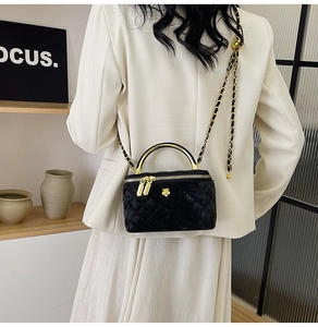 Detail of black quilted velvet camera bag with gold logo and leather-woven chain strap