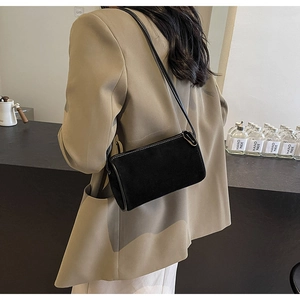 Minimalist black suede shoulder bag with white contrast stitching detail shown on model