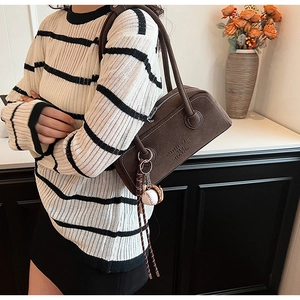 Detail of a dark brown suede underarm bag featuring a vintage baseball keychain accessory