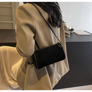 Detail of a black suede baguette bag with fine stitching on a khaki blazer