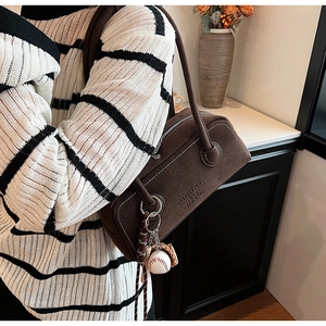Detail of dark brown suede shoulder bag with contrast stitching and baseball pendant