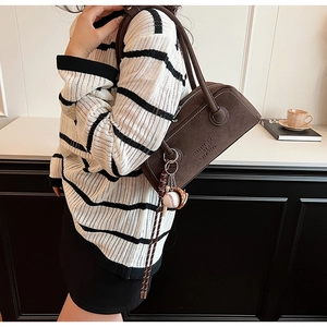 Detail of a brown suede Boston bag featuring double round handles and a baseball charm