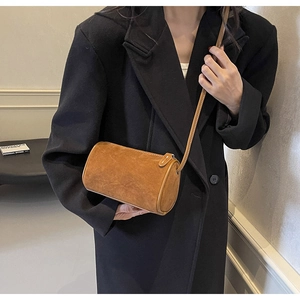 Detail of a brown cylindrical crossbody bag in matte suede texture shown on a model