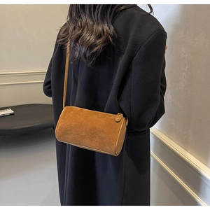 Model wearing a camel suede cylinder shoulder bag with minimalist crossbody strap detail