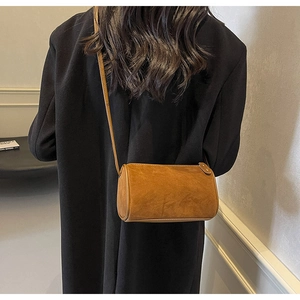 Detail view of a vintage brown cylindrical crossbody bag on a black wool coat backdrop