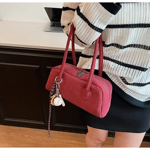 Detail view of red suede texture and baseball charm on minimalist shoulder bag