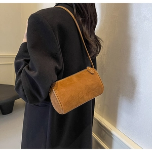 Macro detail of brown suede cylinder shoulder bag on black blazer with leather texture