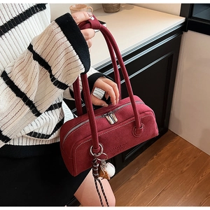 Detailed macro view of deep red suede handbag featuring silver zippers and baseball charm