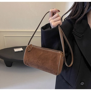 Close-up of a brown suede cylinder shoulder bag with metal zipper on a black coat