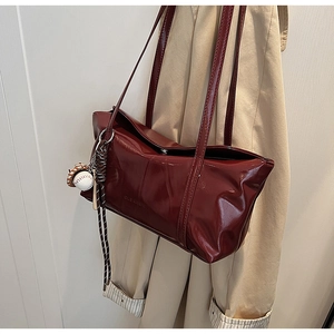 Detail of burgundy glossy leather handbag with baseball charm on beige trench coat