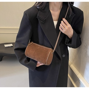 Detail view of dark brown suede cylinder bag with contrast stitching on black blazer