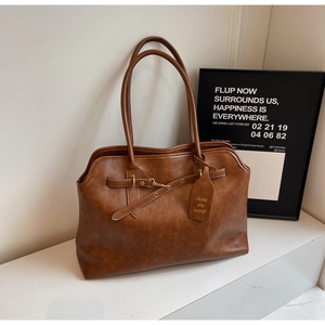 Close-up of vintage brown leather tote bag with metallic buckle and decorative tag
