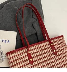 Detail of red houndstooth tote bag fabric with red shoulder strap and golden rivets