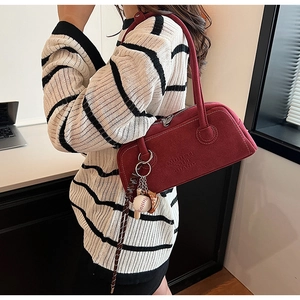 Detail of burgundy shoulder bag with baseball charm and striped strap over sweater