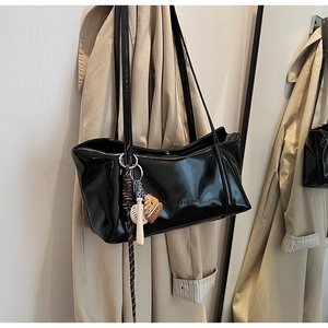 Close-up of black patent leather shoulder bag with CLEA ROX logo and baseball charm