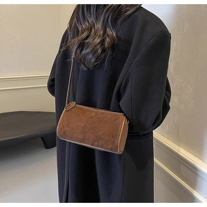 Detail view of a retro dark brown suede cylinder crossbody bag worn on a model's shoulder