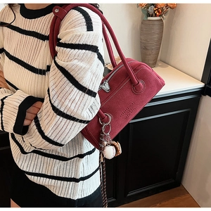 Close-up of wine red suede shoulder bag with silver zipper and baseball glove charm