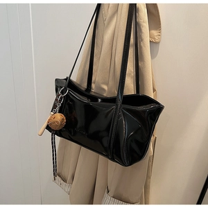 Close-up of black glossy patent leather tote bag with slim straps on a beige trench coat