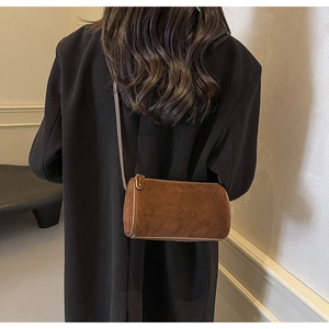 Close-up of a brown suede cylinder bag worn on a shoulder against a black blazer