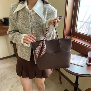 Detailed view of deep brown pebbled leather tote bag with stylish red silk scarf handle accessory