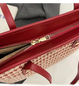 Detail of a red and white tweed tote bag showing a smooth gold metal zipper and red leather edge