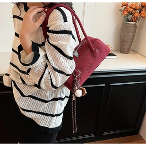 Detail view of burgundy underarm bag with unique baseball charm and embossed branding