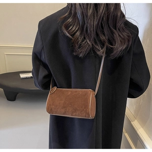 Close-up of brown suede cylinder crossbody bag styled on a elegant black coat