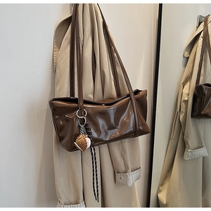 Close-up of brown glossy shoulder bag with baseball charm and Cleanok brand logo