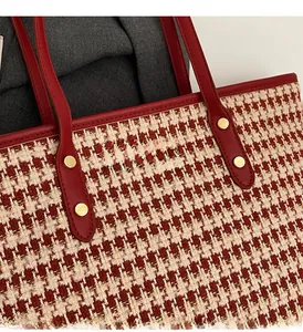 Detail of red houndstooth tote bag with leather straps and gold metal rivet hardware
