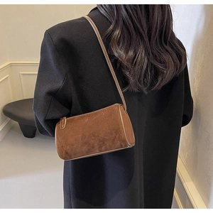 Detail view of a brown suede barrel bag with fine stitching on a black coat outfit