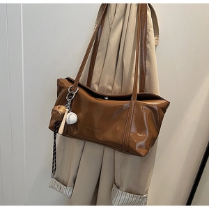 Detail of a brown glossy underarm bag with a baseball charm and clearok logo branding